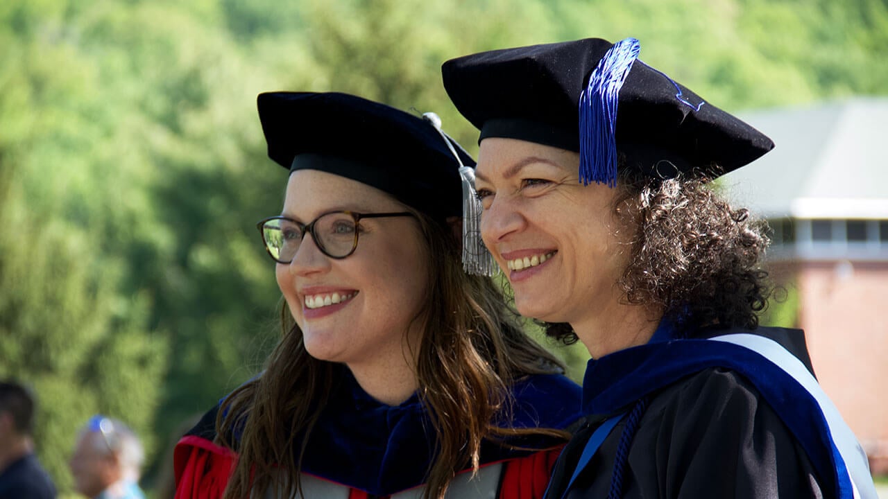 two faculty members pose together looking off to the side and smiling