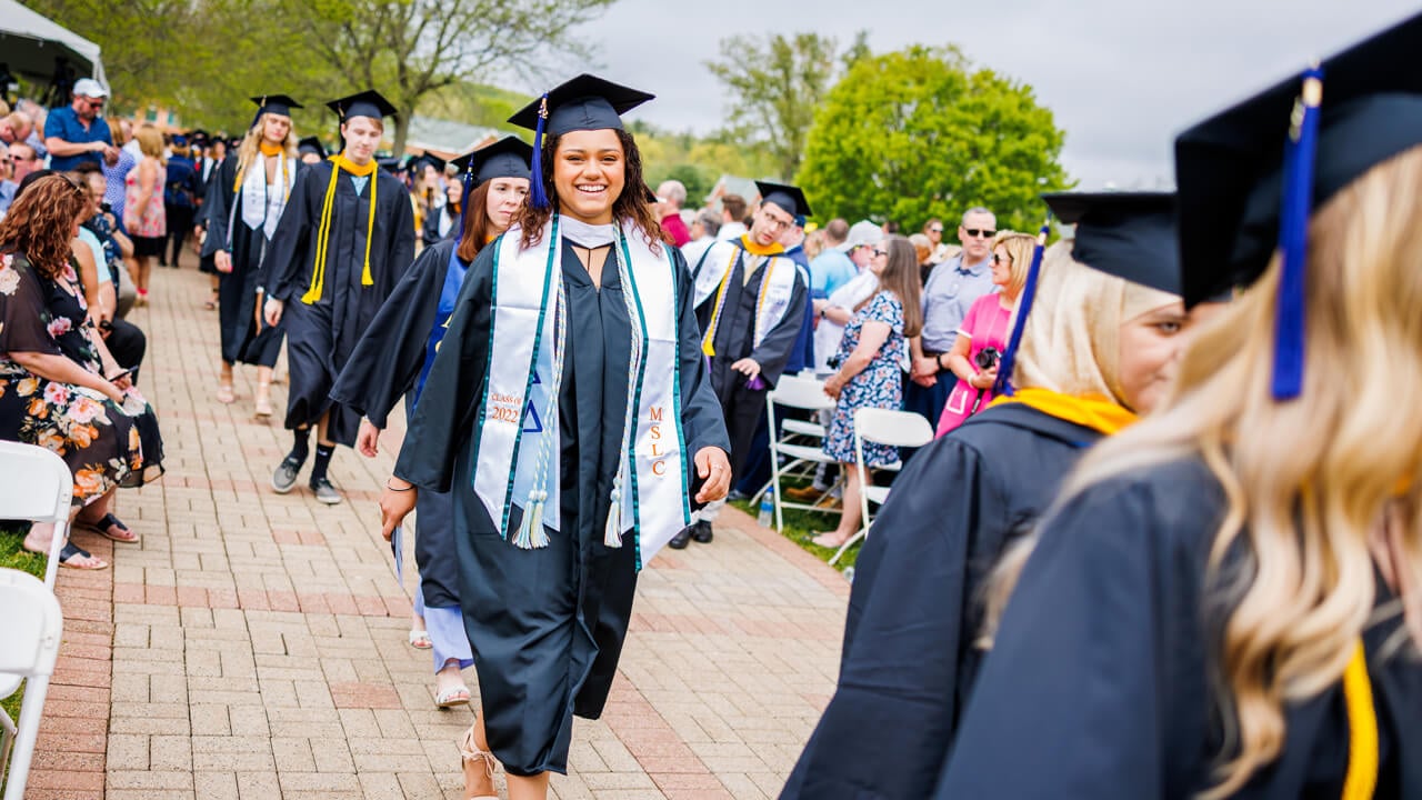 Graduates walk by friends and family as they walk across the quad