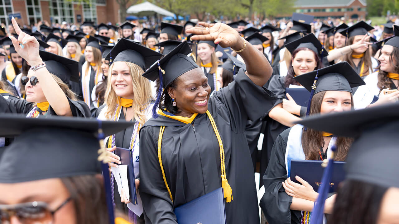 A graduate stands up, smiles and waves