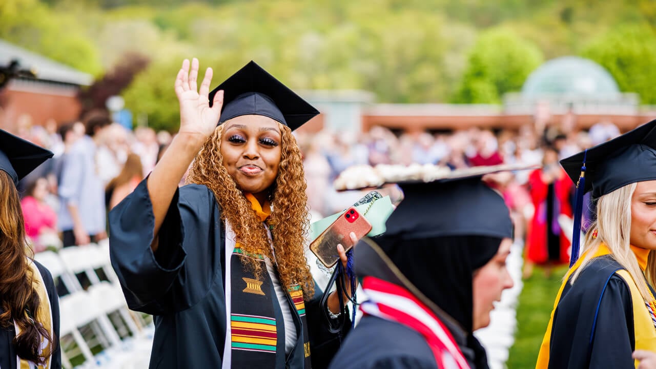 A graduate waves as she walks across the quad