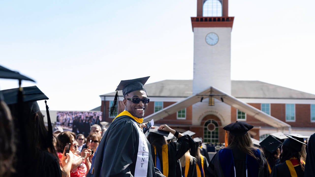 Graduate smiling happily while looking back and the background is Arnold Bernhard library