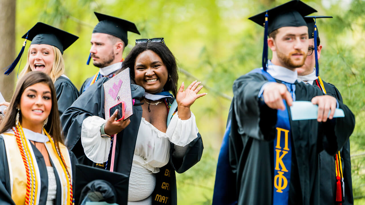 Graduates smile and wave as they wait to process into Commencement