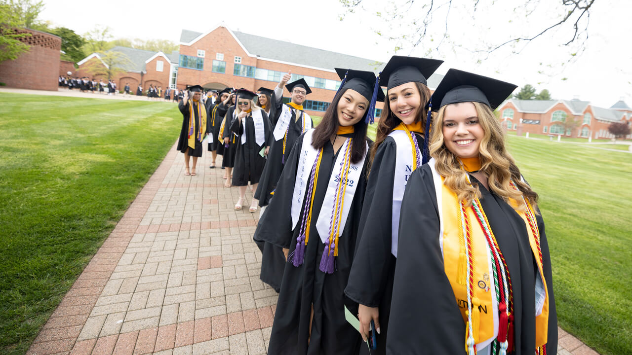 Dozens of graduates walk into the Commencement ceremony on the quad