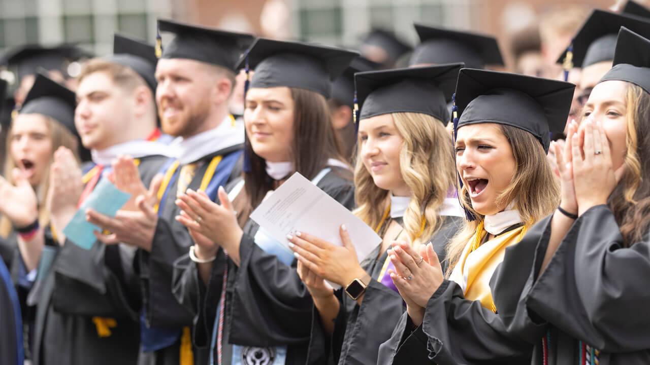 Dozens of graduates clap and cheer during the ceremony