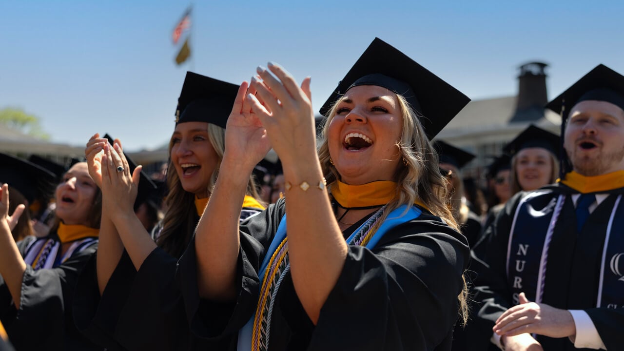 Dozens of graduates clap and cheer in the sun