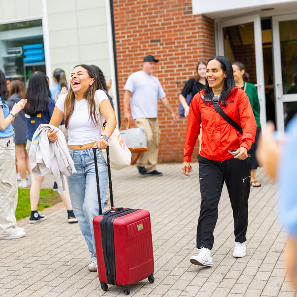 A new student and mom smile as they walk into Orientation while students cheer for them