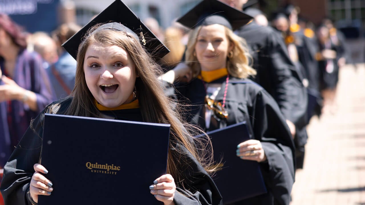 Graduate smiles with diploma walking down quad