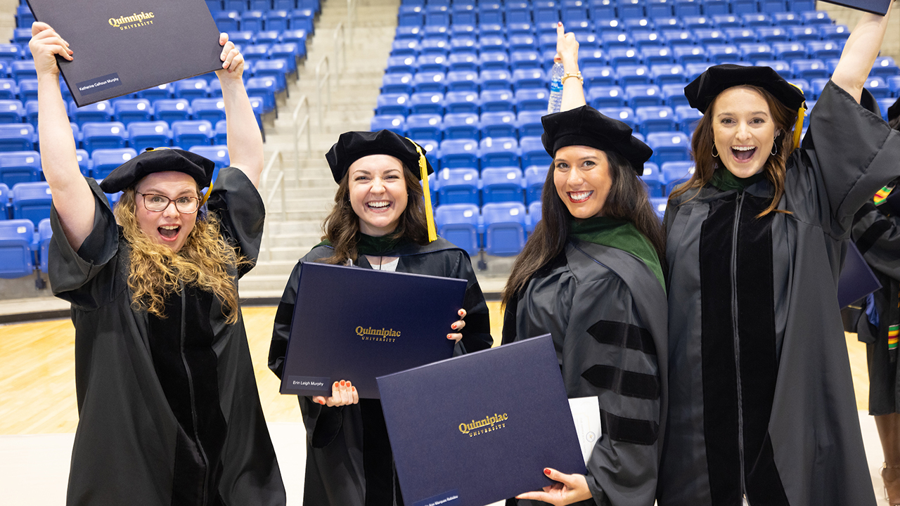 Four graduates smile together while holding up their diplomas