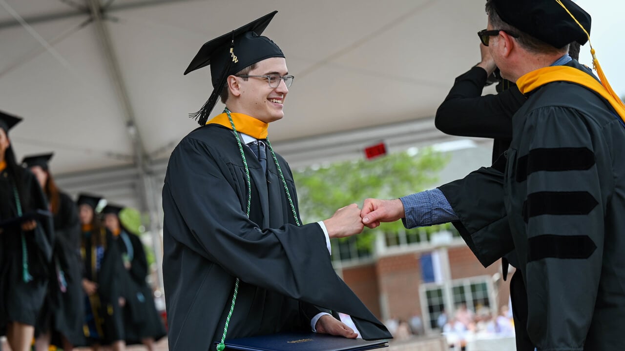 Graduate student gives a fist bump on stage