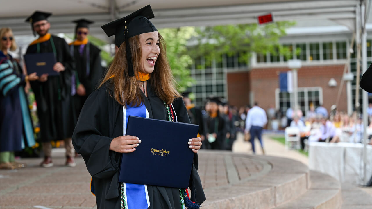 Graduate smiles as she holds her diploma on stage