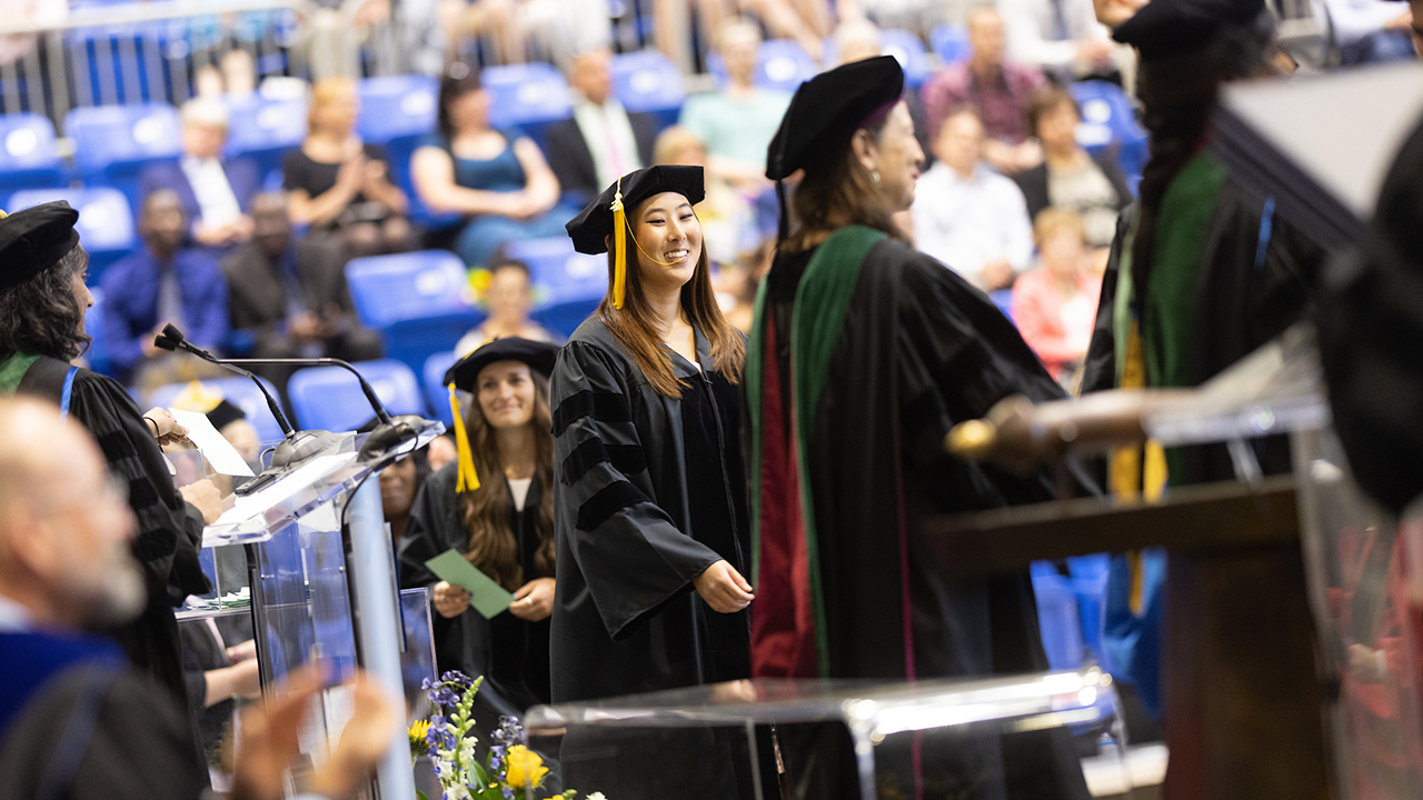 A graduate smiles as they cross the stage to get their diploma