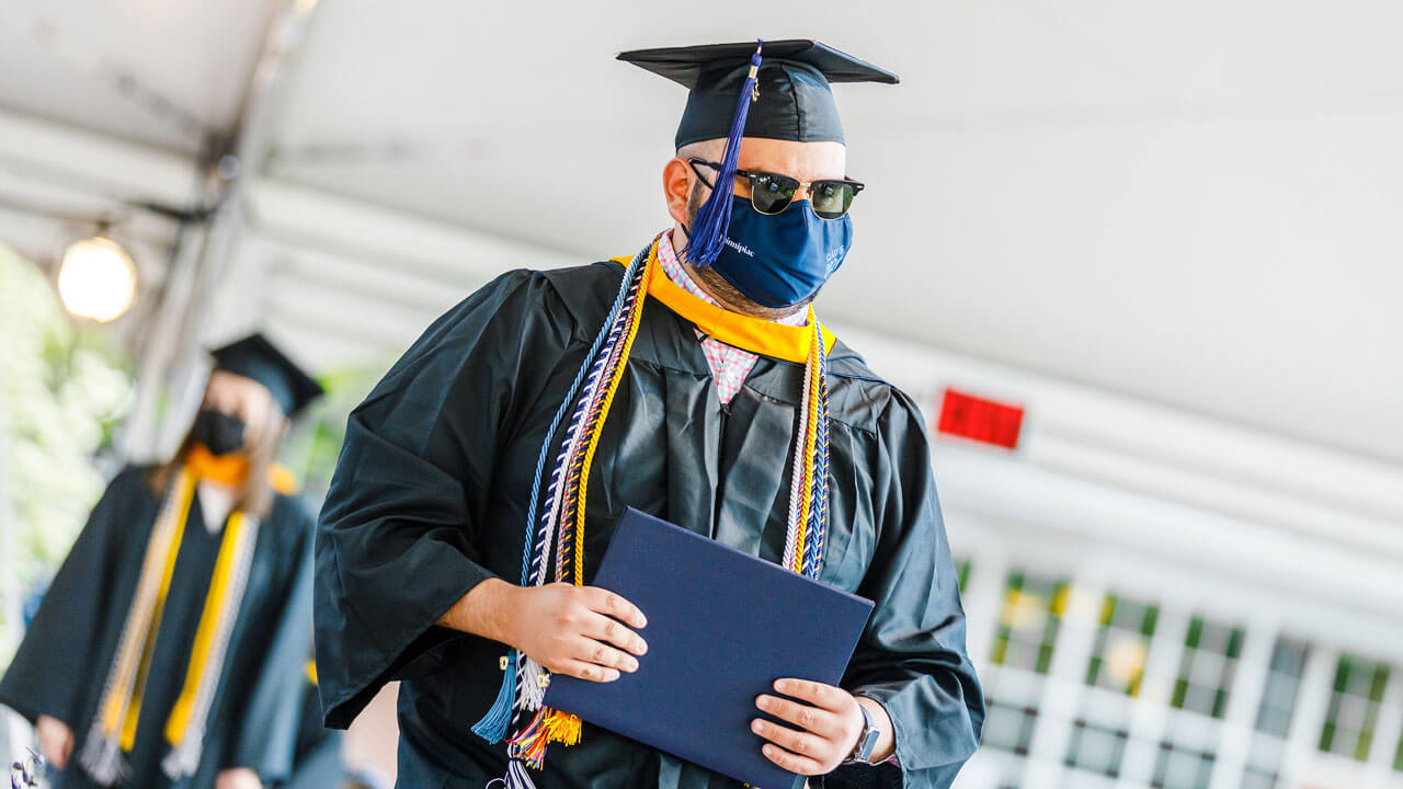 Graduate student walking across the stage carrying their diploma