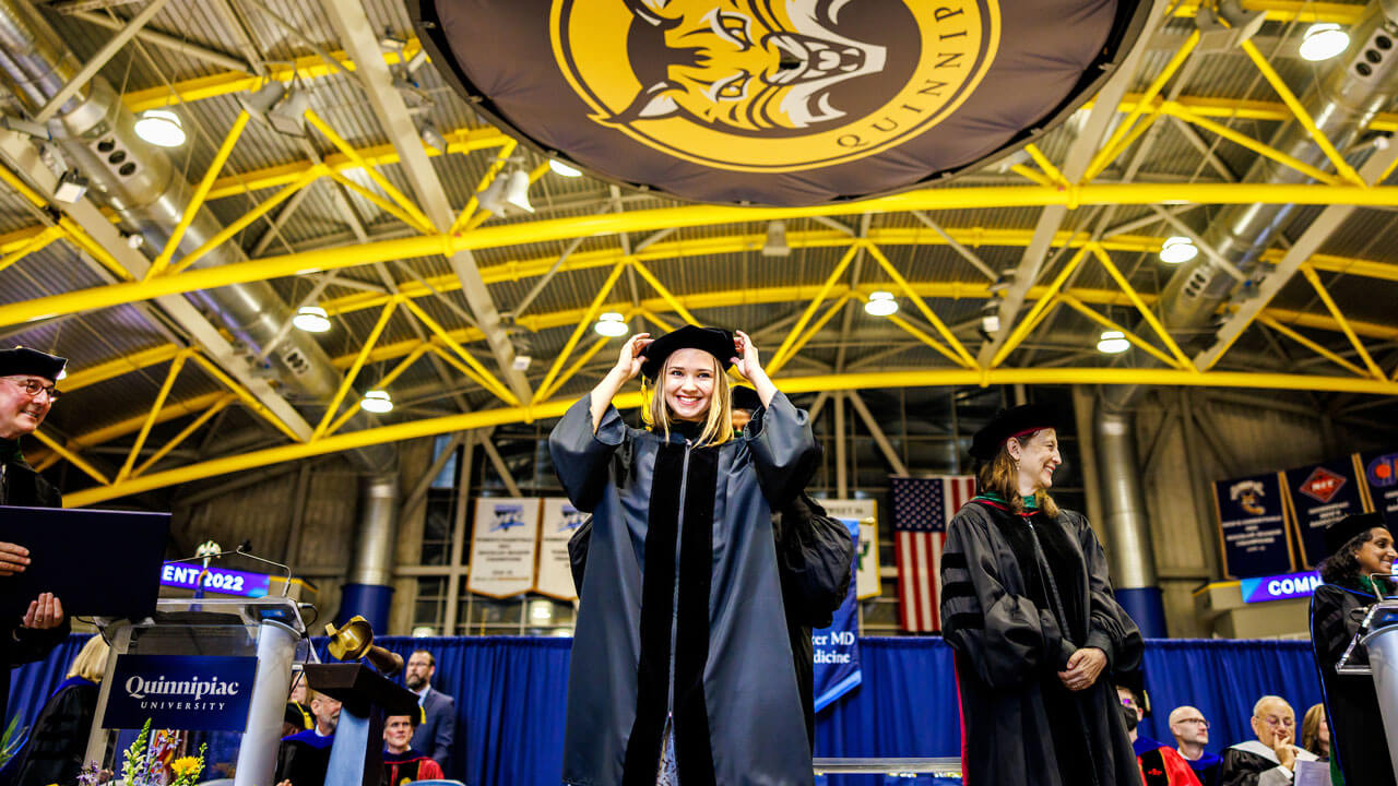 Graduate student fixing cap on the stage and underneath the bobcat sign at commencement