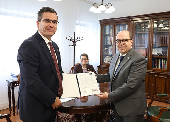 Óbuda University Rector Levente Kovács shaking hands with Dean of the School of Computing & Engineering Taskin Kocak. Provost Debra Liebowitz sitting at the agreement table.