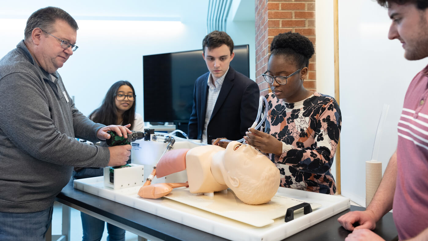 A student shows her project to a professor and classmates during projects day.