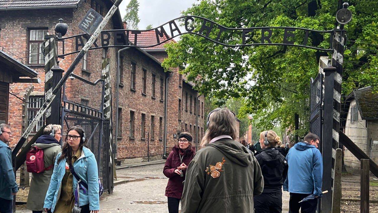 Students listening to tour guide in front of black fence