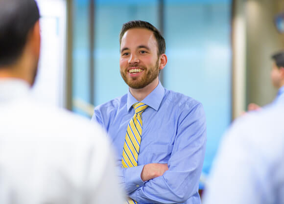 A student in a shirt and tie smiles and talks with people during a conference