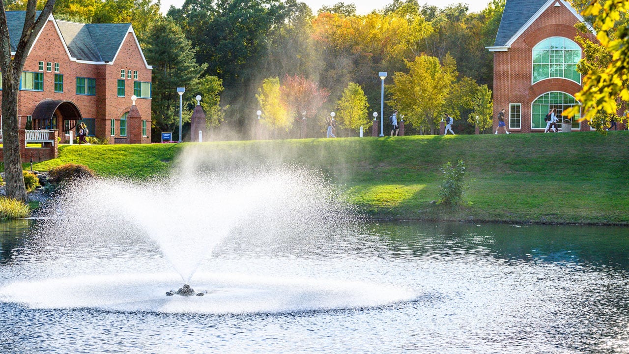 Fountain sprinkling water over pond as students walk to class in the distance