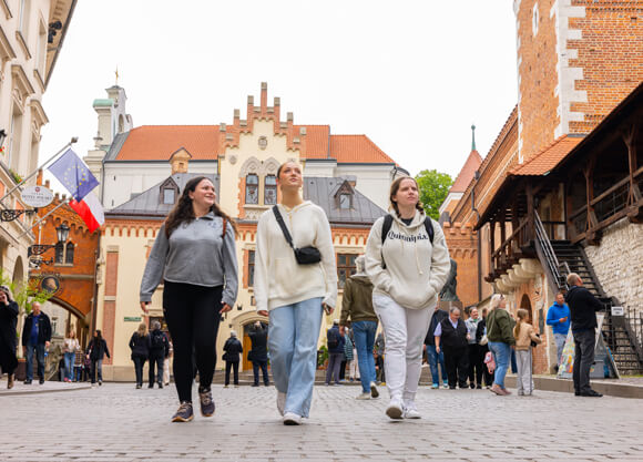 Three Quinnipiac students walk down a street with historic buildings in Krakow, Poland