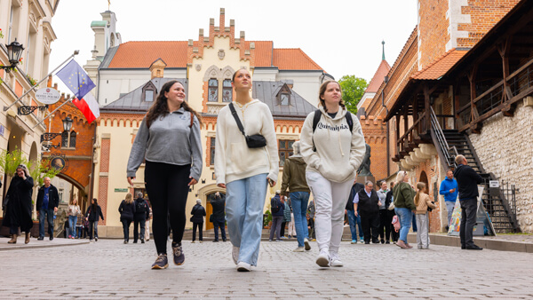 Three Quinnipiac students walk down a street with historic buildings in Krakow, Poland