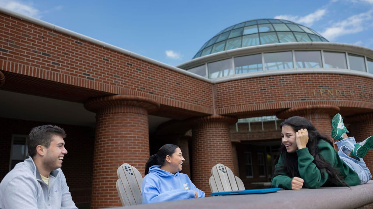 Students sitting out by the school of business, talking to each other