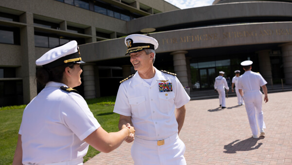 A student in a military uniform shakes hands with the director for veterans affairs outside