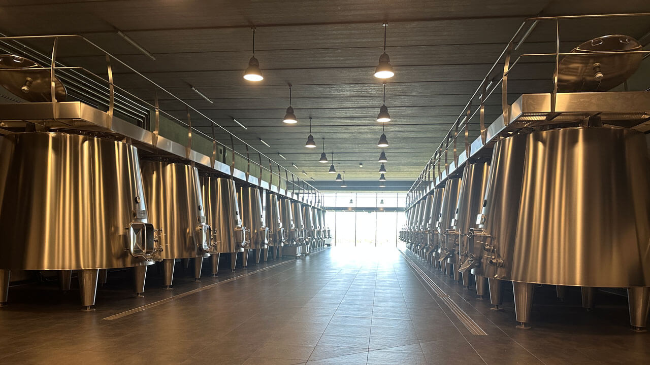 A row of emptied silver metal wine vats leading to a window