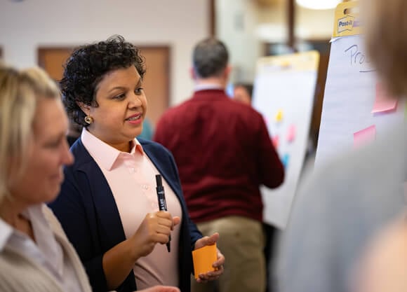 Individuals discuss in front of a board holding a marker