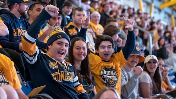 Hundreds of students in national champions gear cheer from the stands at the hockey arena