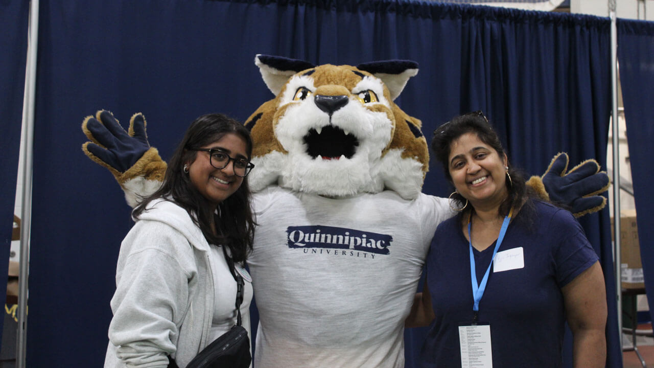 Boomer raises their arms as they take a photo with a Quinnipiac Orientation family