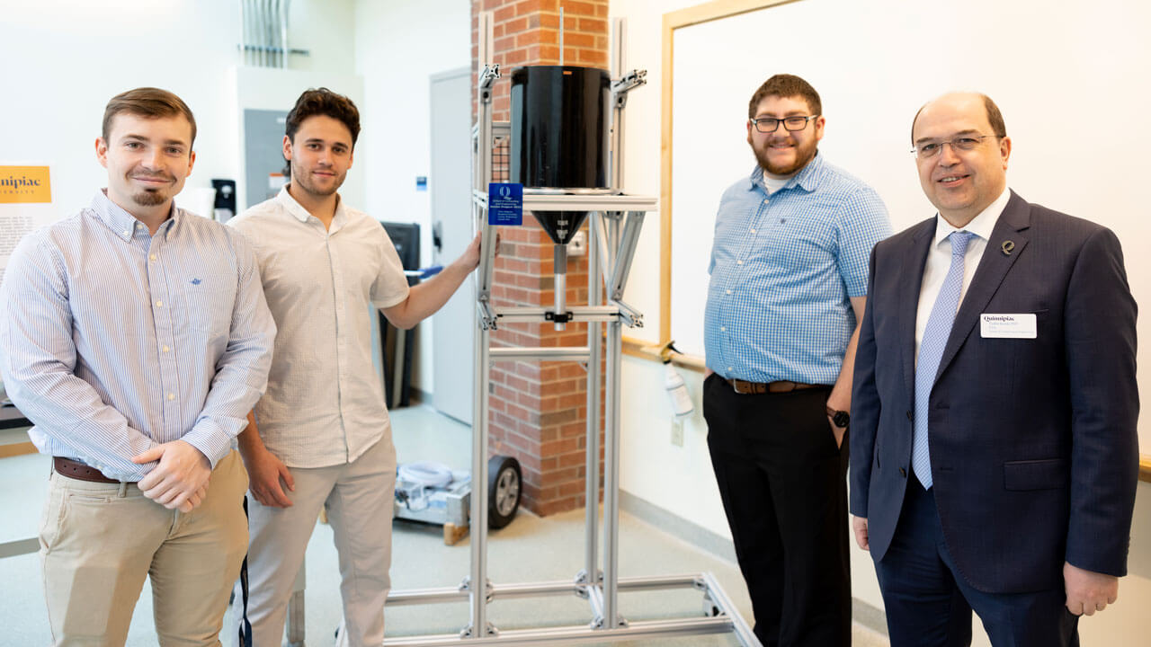 Students pose with their professor and project exhibit.