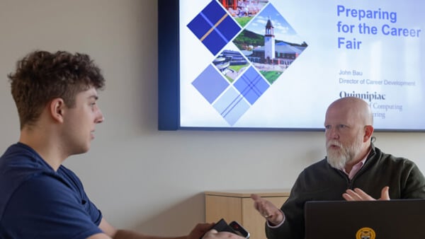 A male student sitting at a table speaking with a male professor