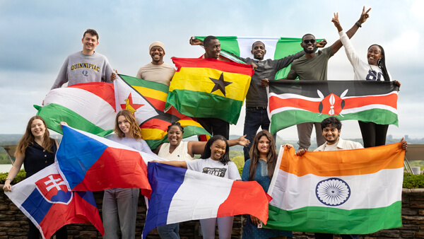 A dozen International students hold up their home country flags and pose for an outdoor photo