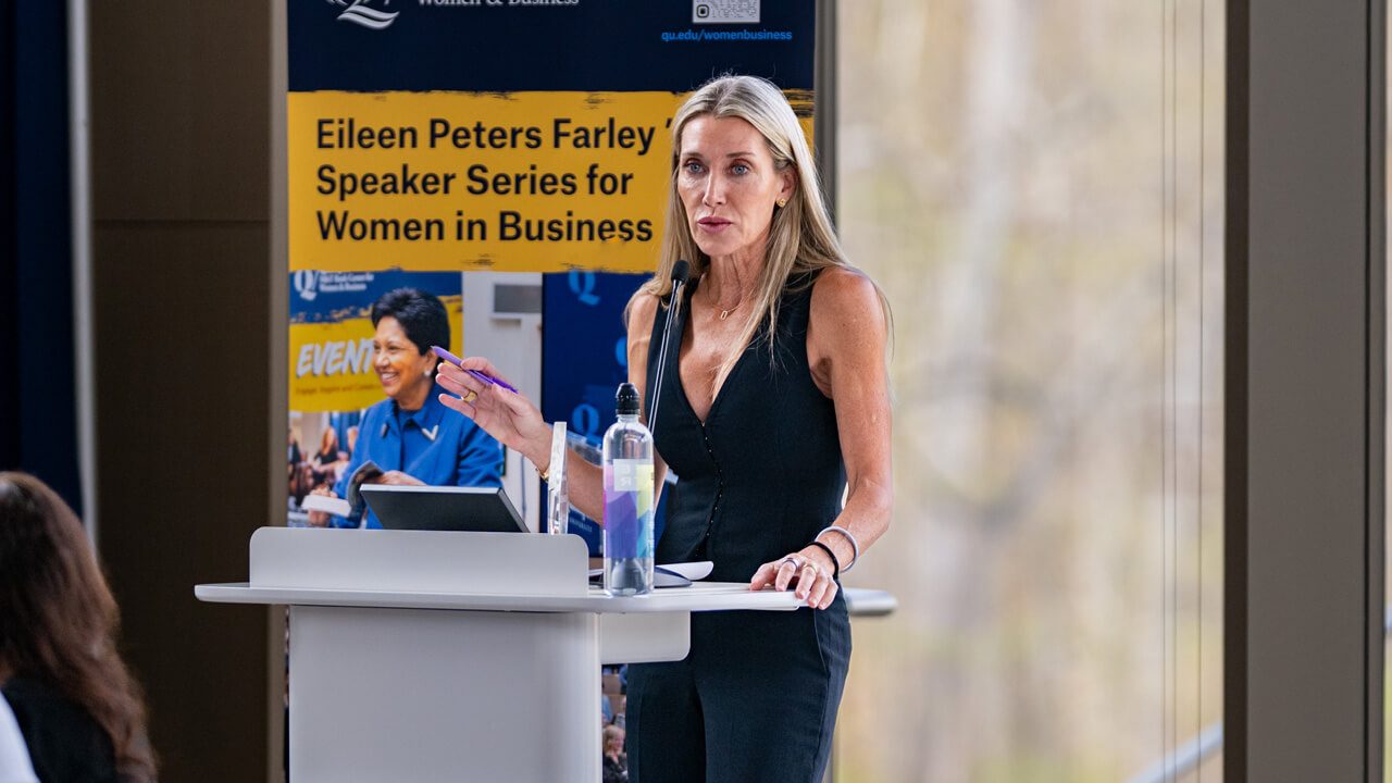 Jessica Geis speaks at a podium in front of a Speaker Series banner.