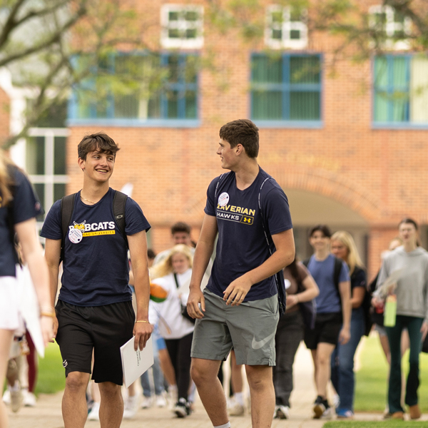 Two students in a group walk and talk down a path on the Quinnipiac quad