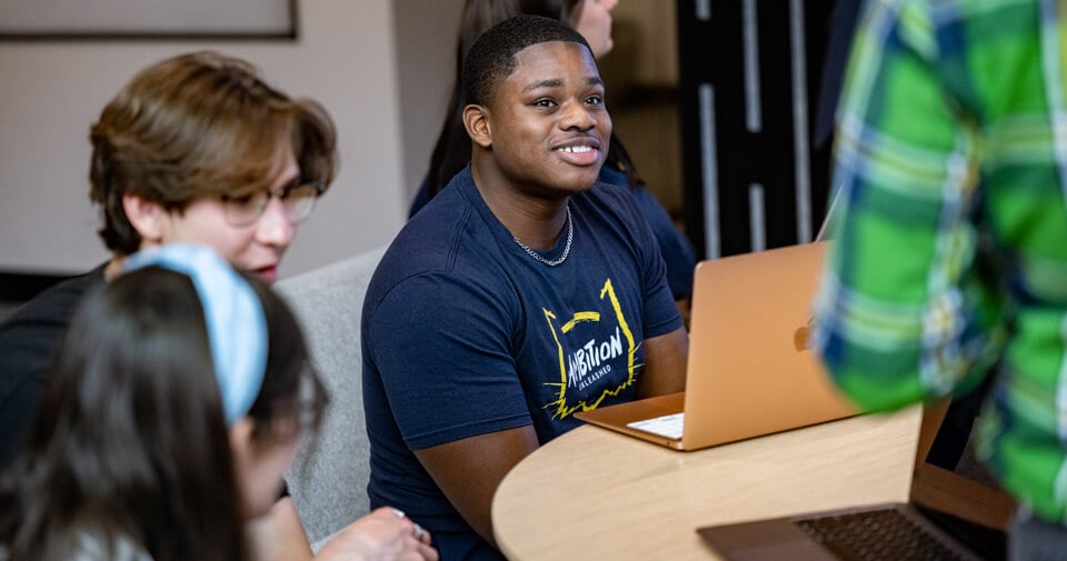 Pre-professional students sit at a desk with computers and speak with a professor