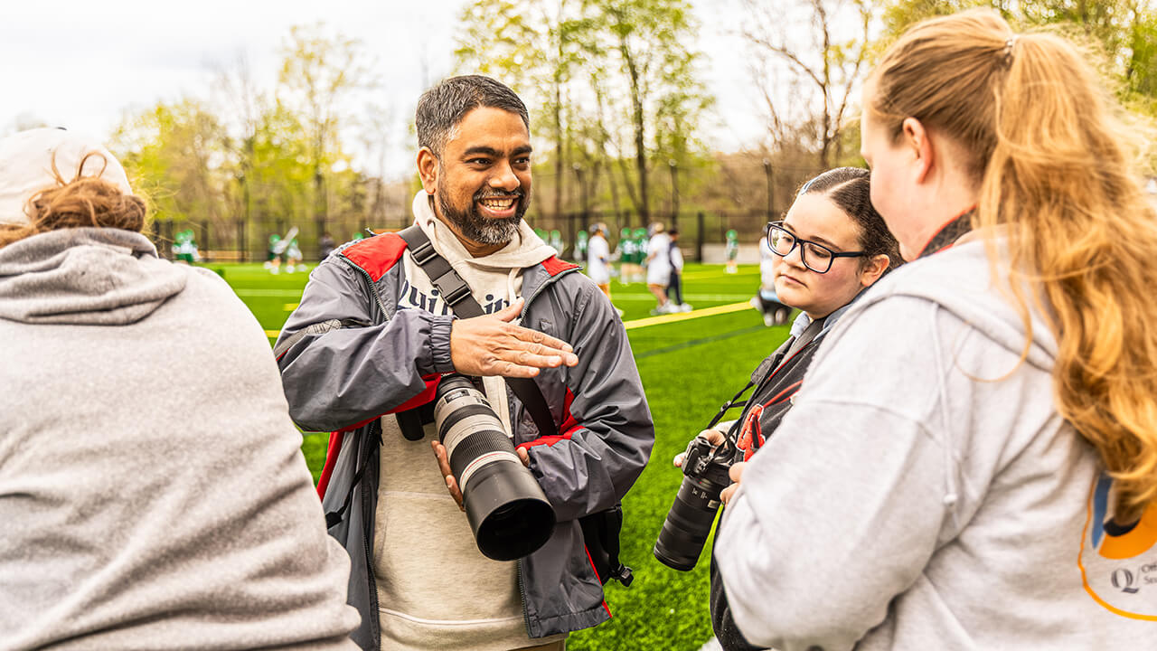 Professor Wasim Ahmad talking to 2 female students, all holding Canon cameras on a Lacrosse field