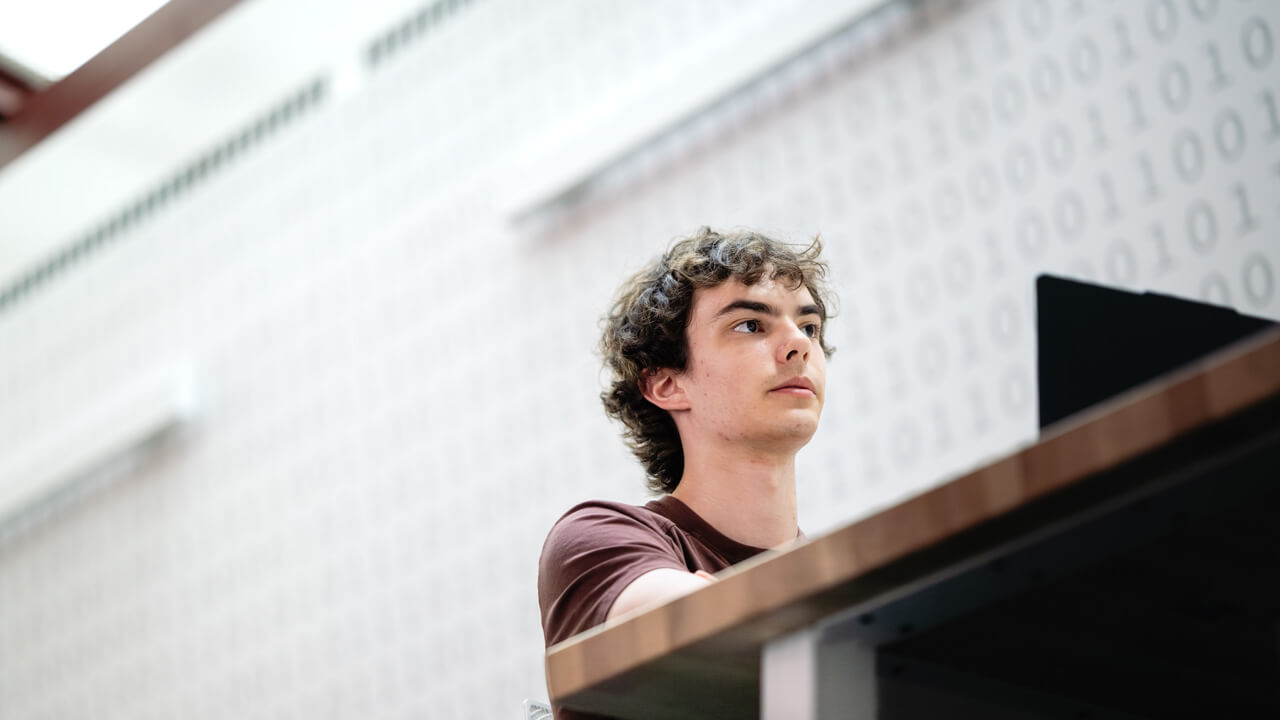 A shot from below of a male student sitting at a table with a laptop.