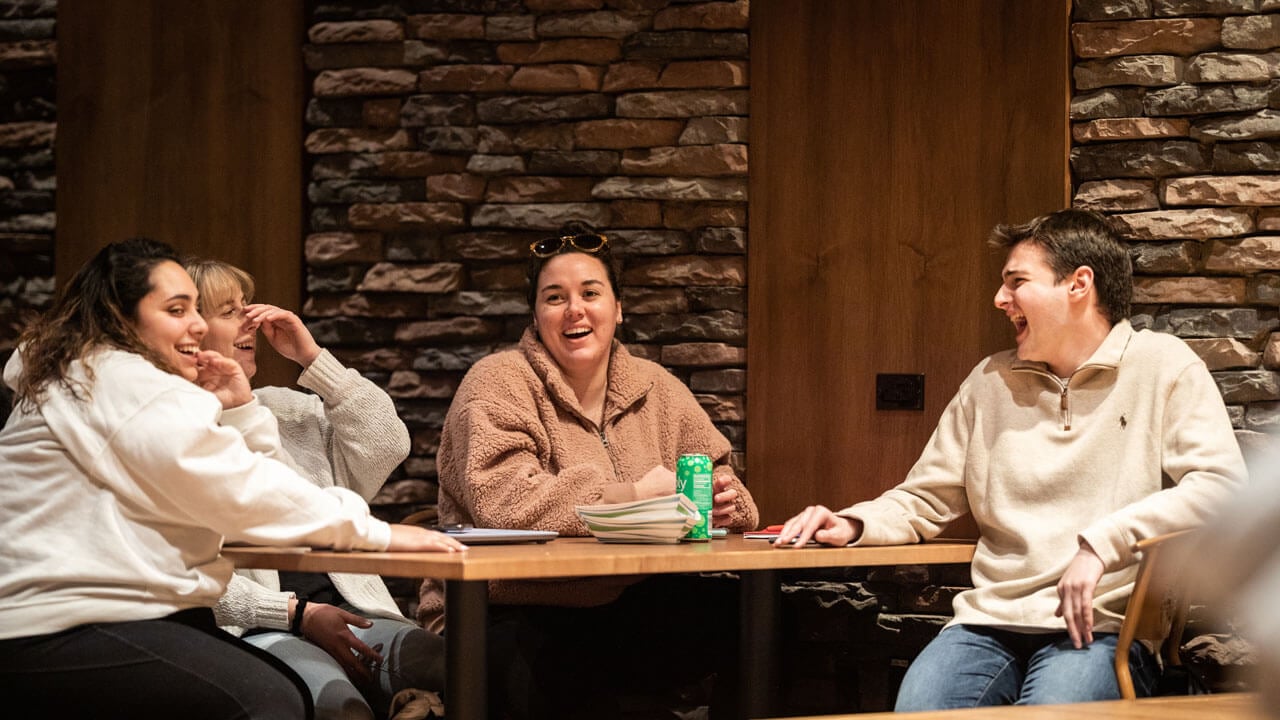 Four students sit at a table laughing and talking in the pub