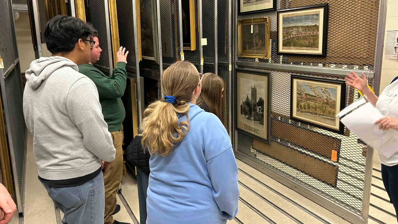 Four students look at a gallery wall of Revolutionary War–era art. One is taking a photo.