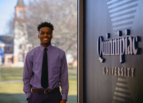 Marcus Pierre stands next to Quinnipiac sign