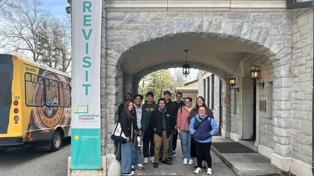 A group of 10 students stands outside the entrance to the Connecticut Museum of Culture and History, alongside a banner reading "Smithsonian Affiliate."
