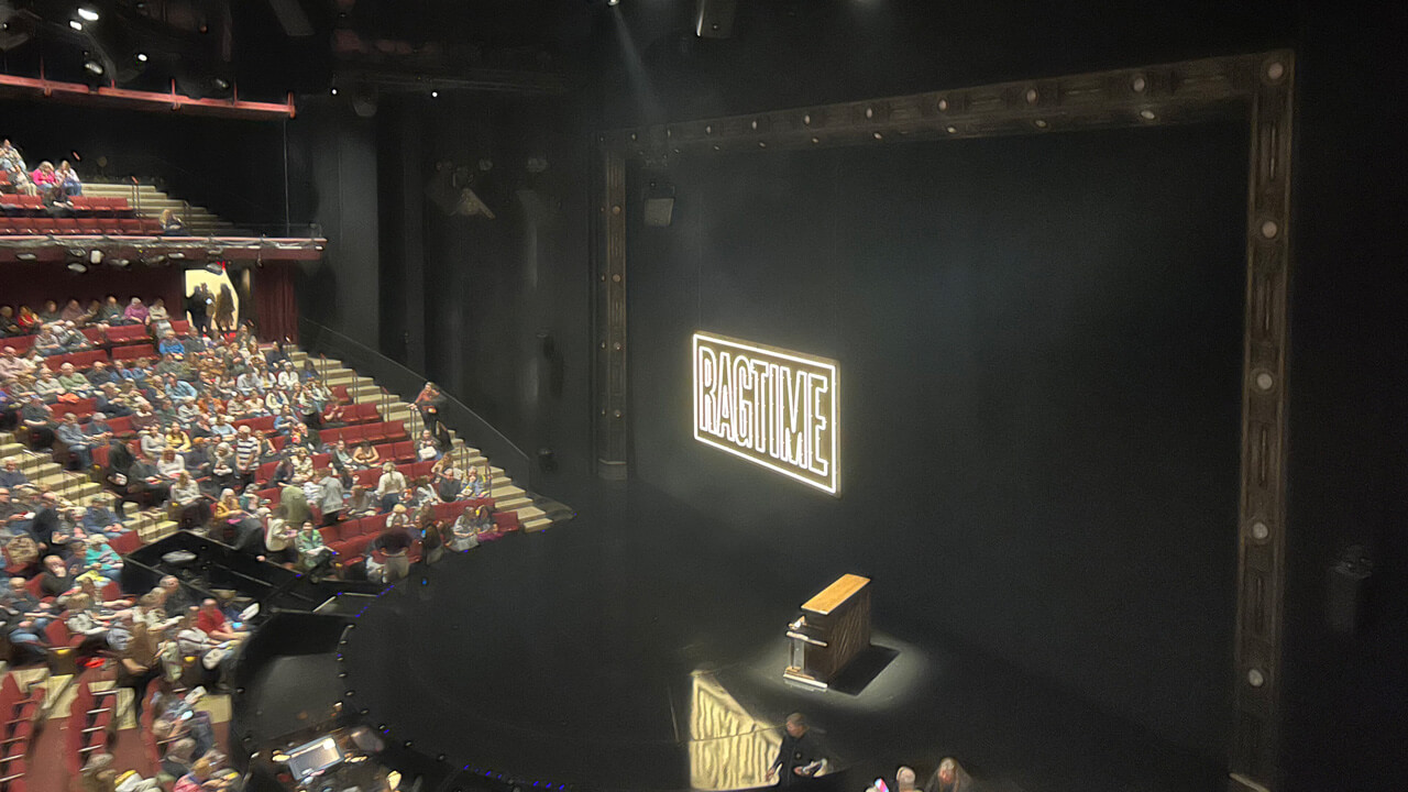 An image of the stage before the show: the word Ragtime lit up, and a piano with a spotlight on it.