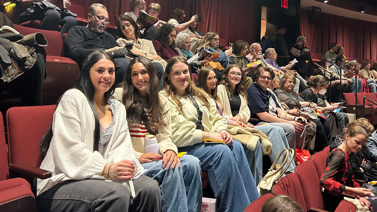 A group of six students smiling, sitting in a row in the theatre.