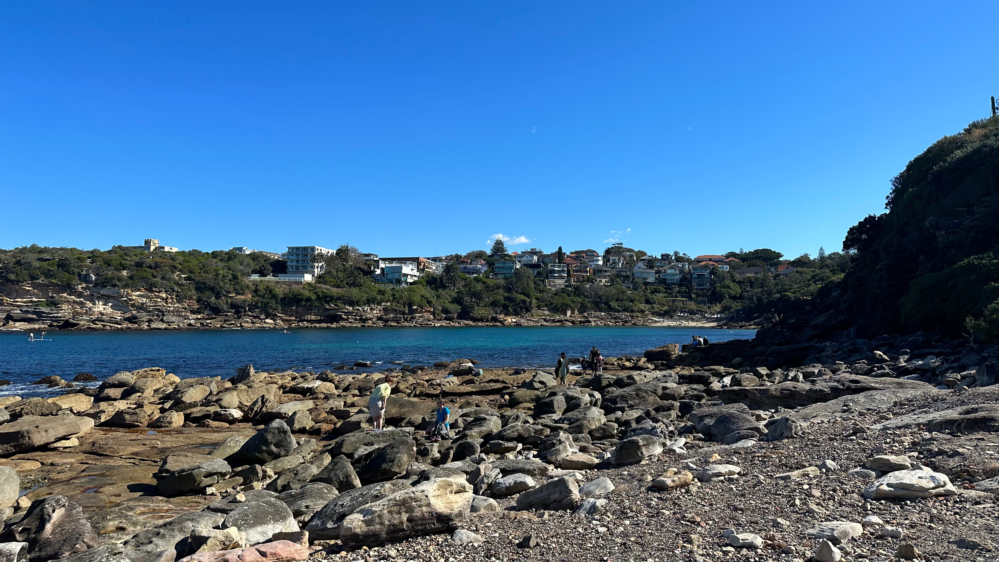 People walking over big boulders and rocks with a river in the background