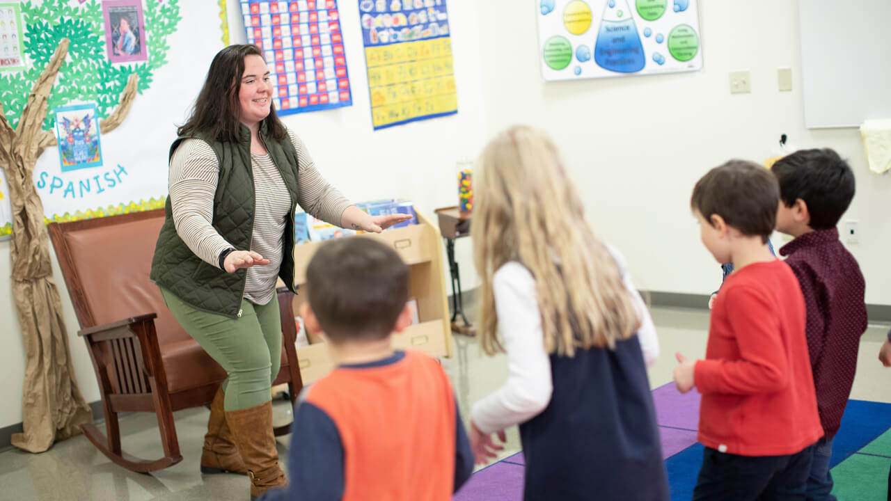 An education student leads a group of children in an activity in a classroom