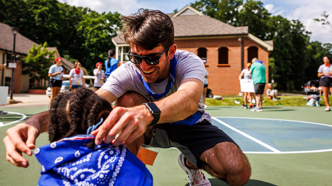 Student places a bandana on a child at camp