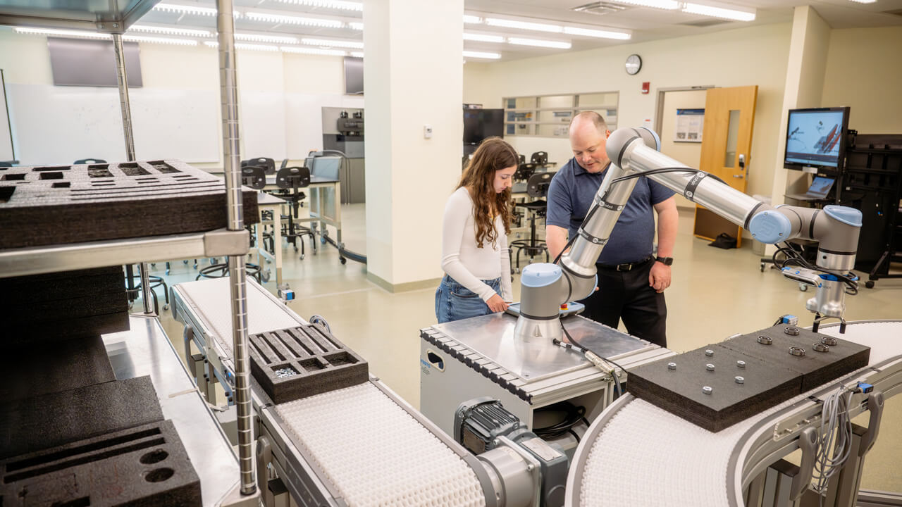 A female student and a professor look at a piece of industrial engineering equipment.