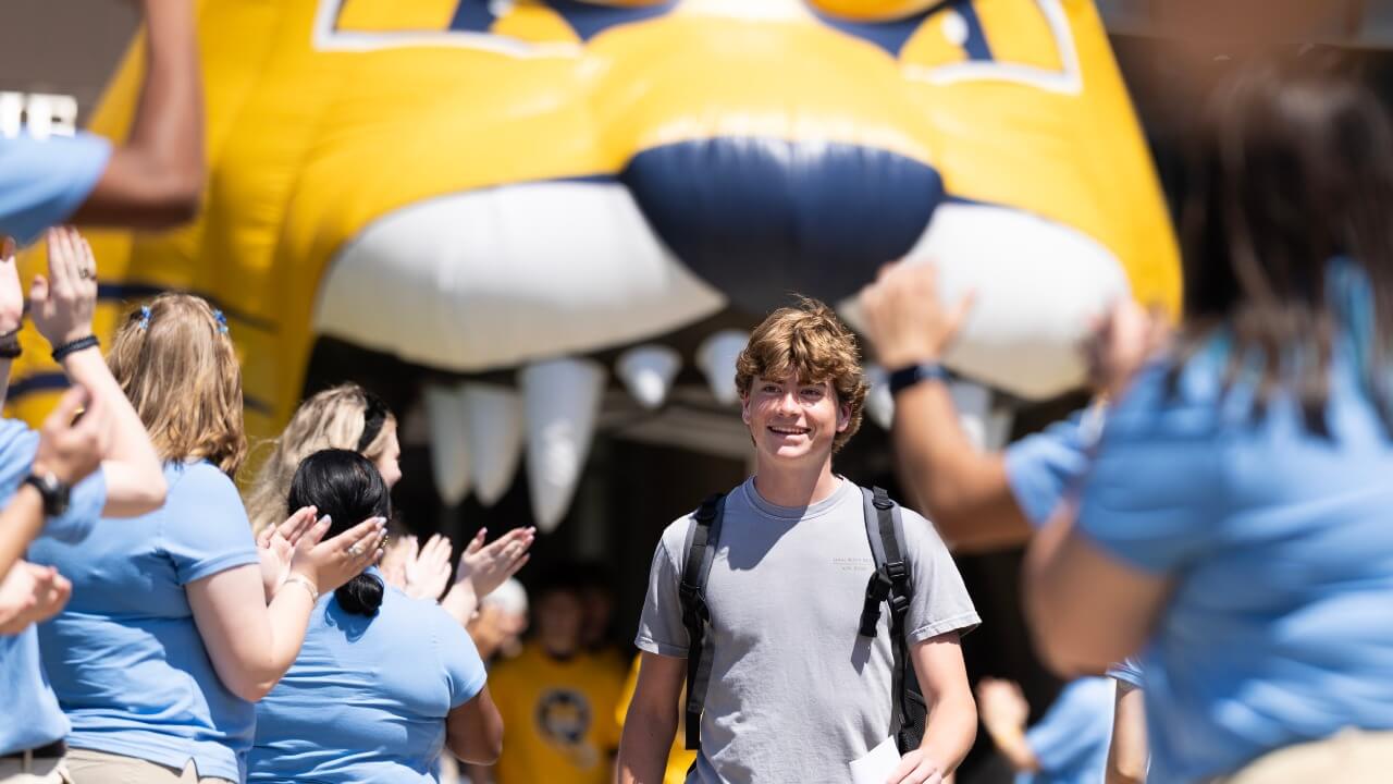 A student smiles as he walks beneath an inflated Bobcat and Orientation Leaders clap