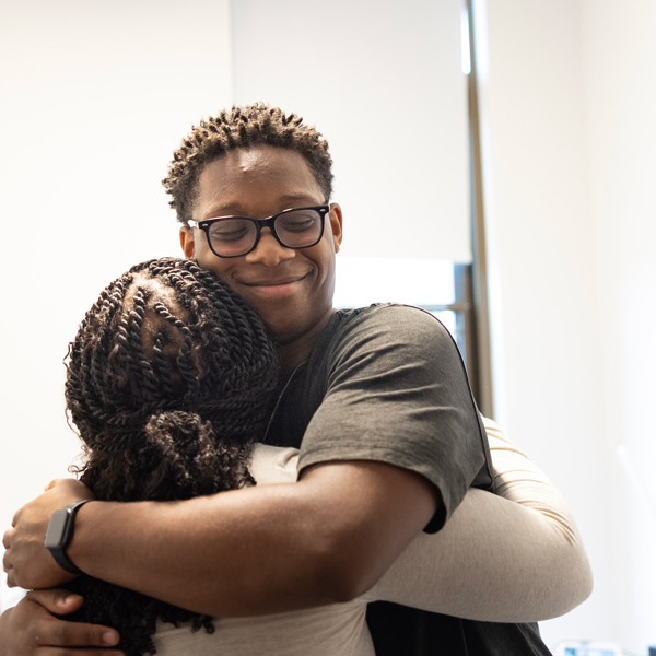 A new student smiles as he hugs his loved one in his new dorm room
